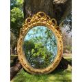 A French Rococo Style Ornately Carved and Gilded Oval Bevelled Mirror