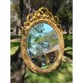 A French Rococo Style Ornately Carved and Gilded Oval Bevelled Mirror