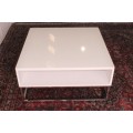 A stunning and modern white square coffee table with a magazine/ book shelf on chromed table legs