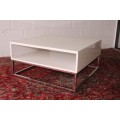A stunning and modern white square coffee table with a magazine/ book shelf on chromed table legs
