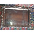 A STAINLESS STEEL RECTANGULAR WITH AN ORNATE DESIGN BORDER SERVING TRAY SOLD AS IS