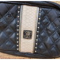 A BLACK GUESS SLING HAND BAG HAS SOME ARE AND TARE ON IT