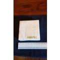 Serviettes: Sealed packet of white drinks serviettes branded Amstel in gold lettering.