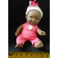 Small African Baby doll in a pink suit. looks like a Berenguer doll