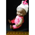 Small African Baby doll in a pink suit. looks like a Berenguer doll