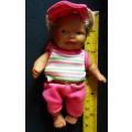 Small light  brown Baby doll in a bright pink utfit with cap. Looks like a Berenguer doll