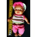 Small light  brown Baby doll in a bright pink utfit with cap. Looks like a Berenguer doll
