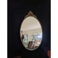 Vintage Gold Oval Mirror With Ornate Detail on top of The Mirror.