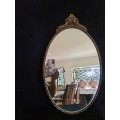 Vintage Gold Oval Mirror With Ornate Detail on top of The Mirror.