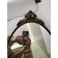 Vintage Gold Oval Mirror With Ornate Detail on top of The Mirror.