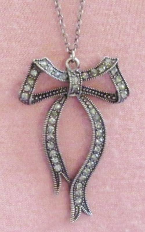 Antique silver tone bow pendant decorated with marcasite stones on a long, thin chain